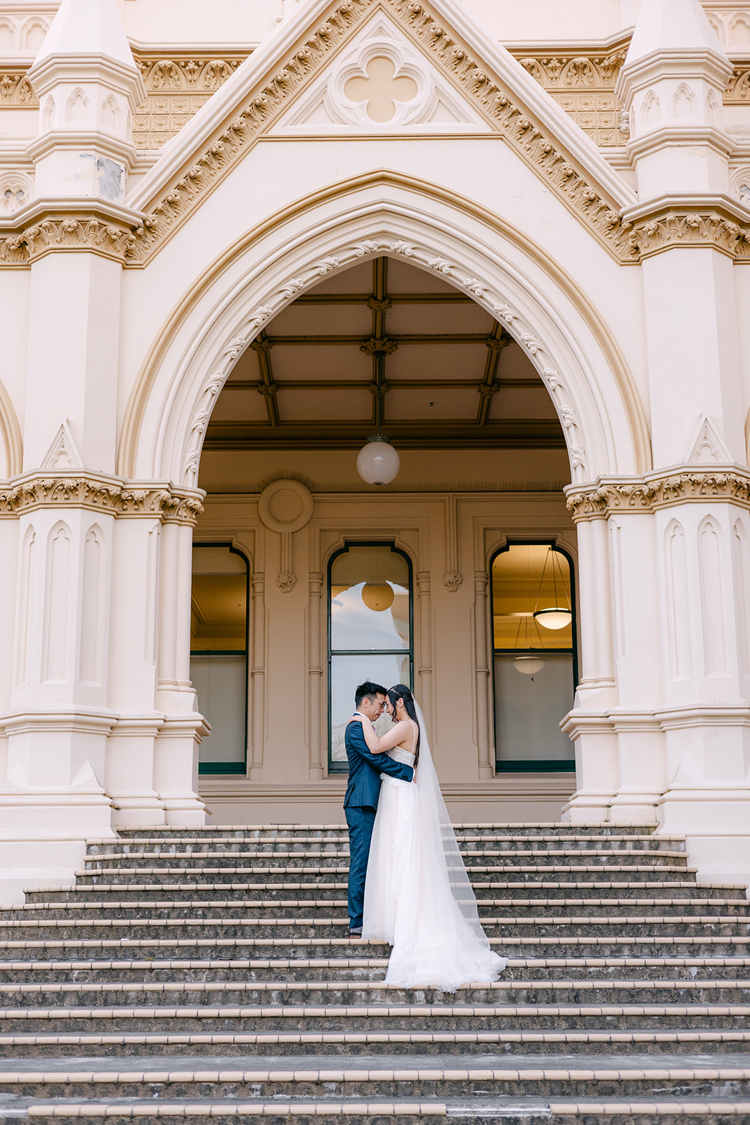 Cornelia and Johnny embracing on the steps of Parliament Library during their Wellington wedding portrait session.