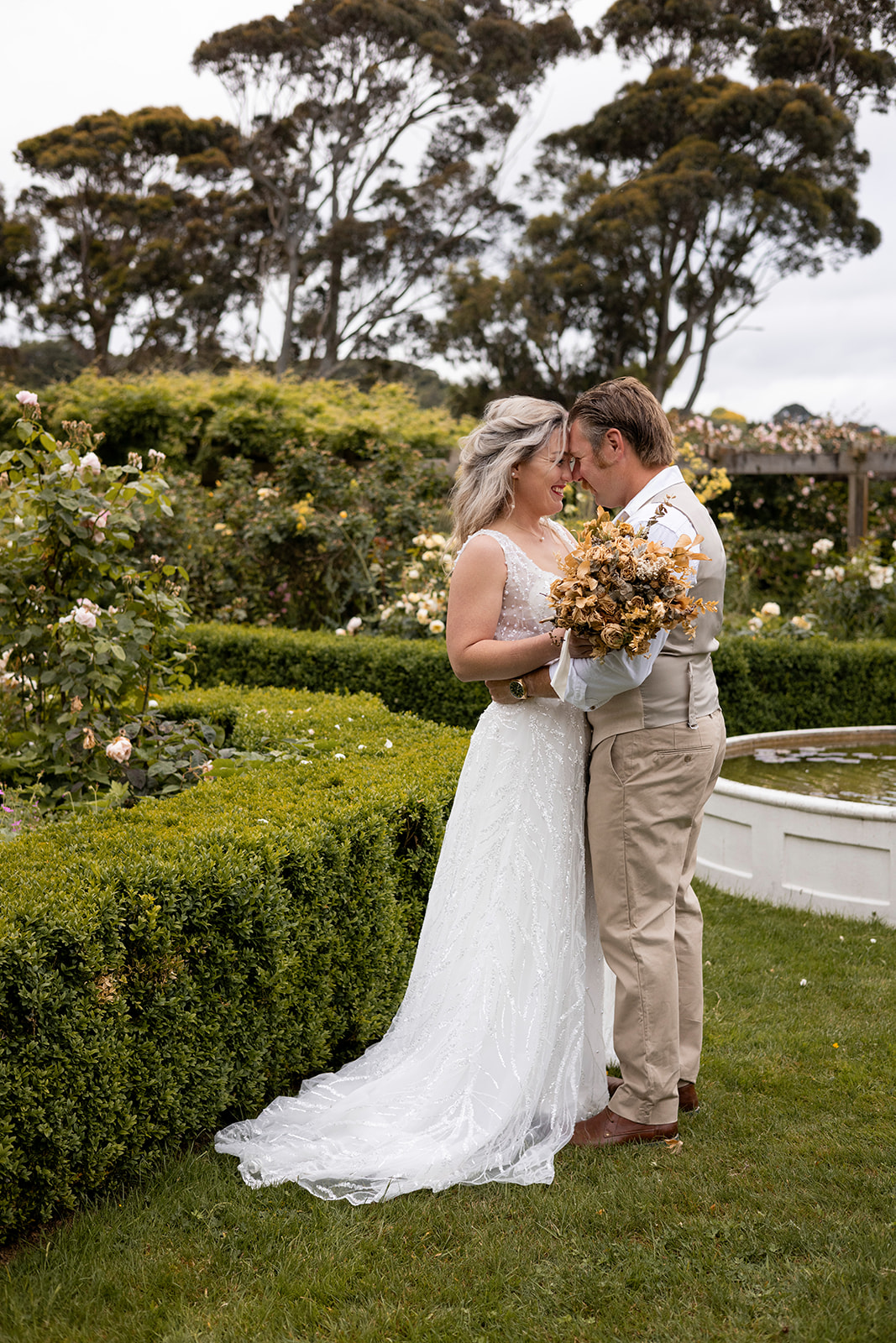 Liz and Elliot in their wedding attire beside the fountain at Greenhaugh Gardens near Palmerston North.