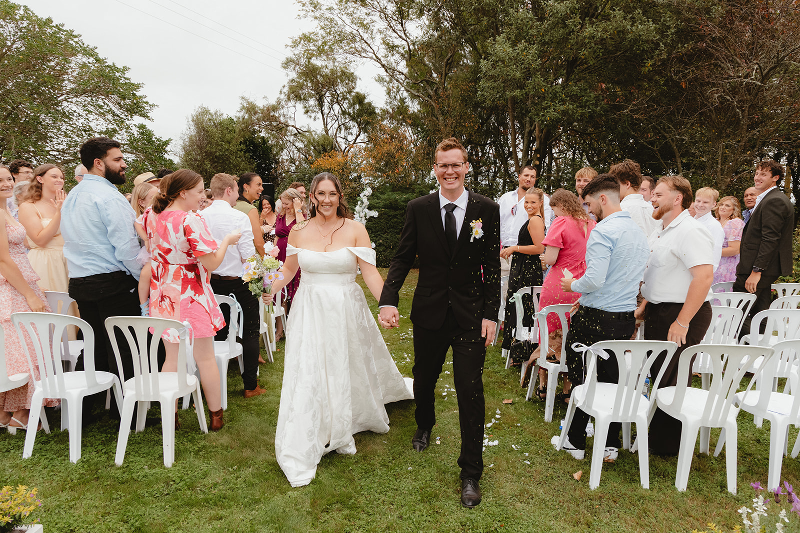 Zoe and Byron walking through their guests during a colourful wedding confetti toss.