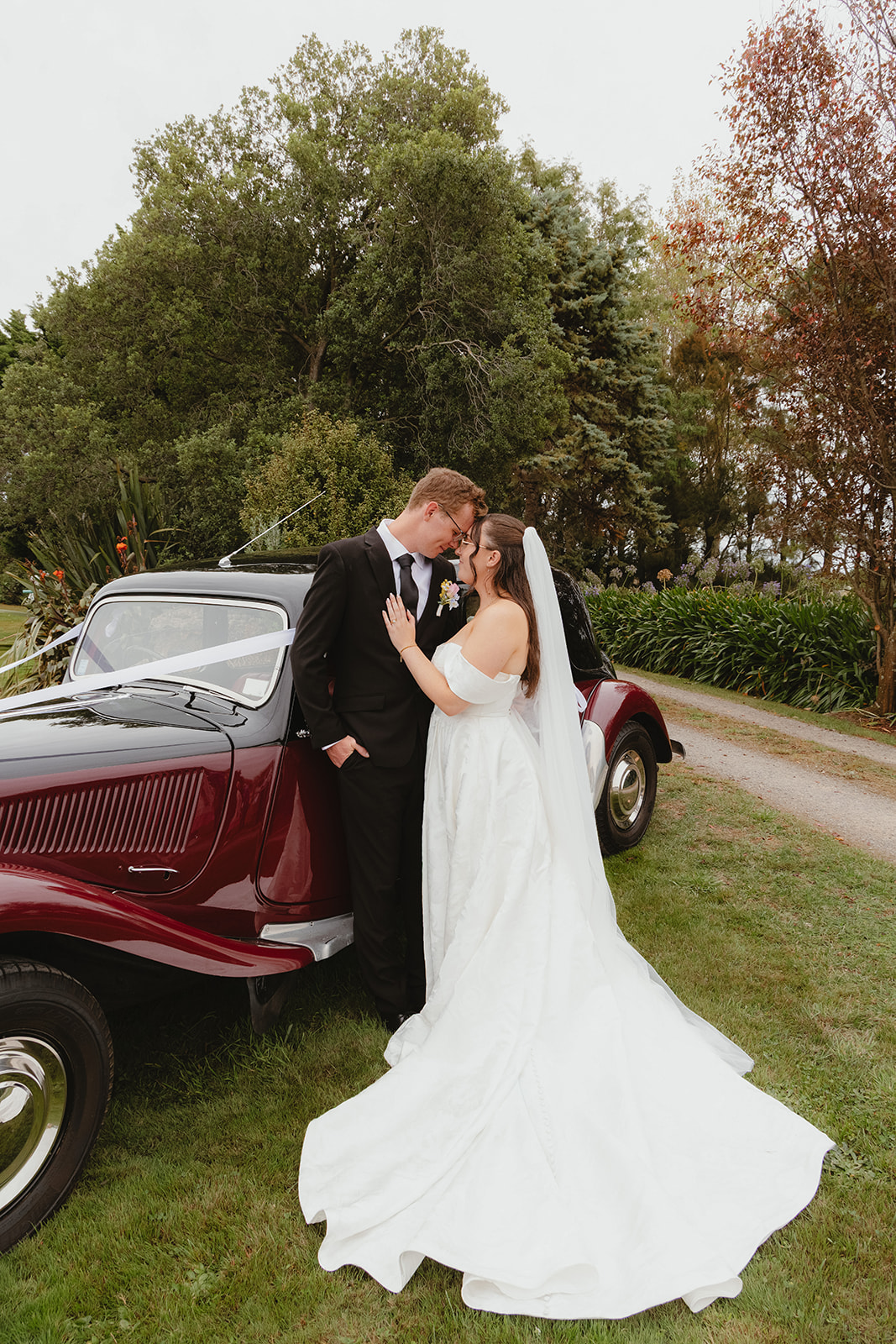 Zoe and Byron kissing beside a vintage car on their wedding day.
